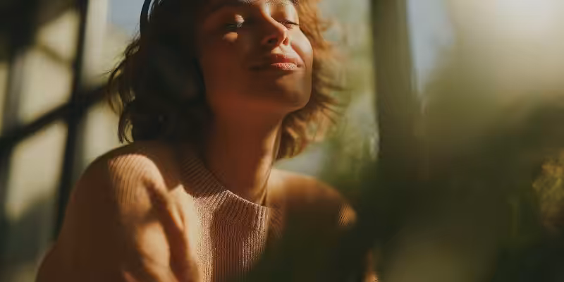 Femme souriante, les yeux fermés au soleil, casque sur les oreilles